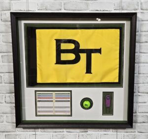 Custom shadow box featuring a yellow and black BT golf flag with a scorecard, branded golf ball, and commemorative golf accessory.